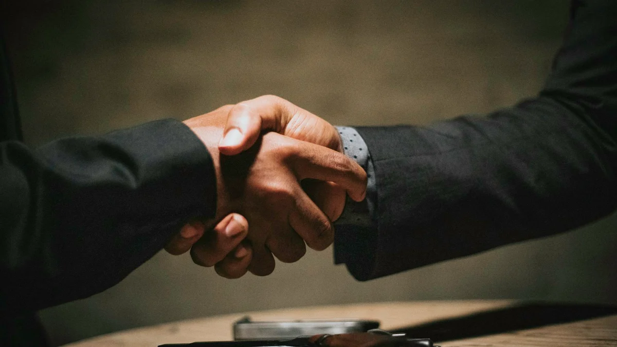 Two people shaking hands over a wooden table after an agreement