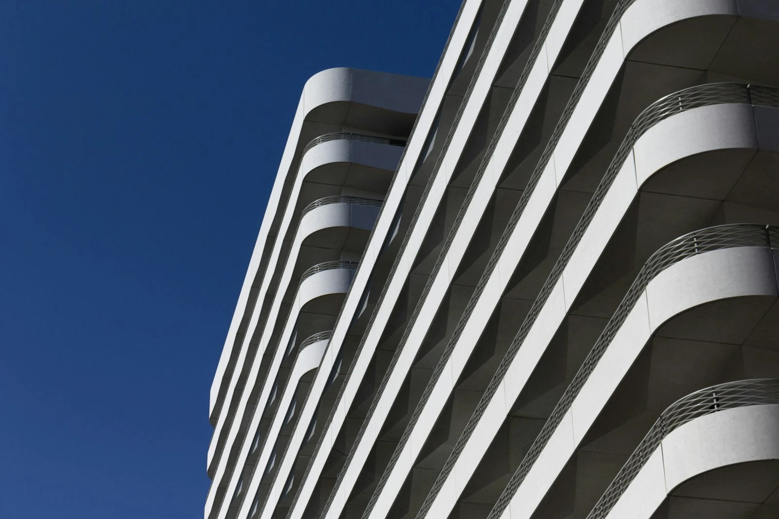 Low-angle view of a white curved apartment building facade against a clear blue sky