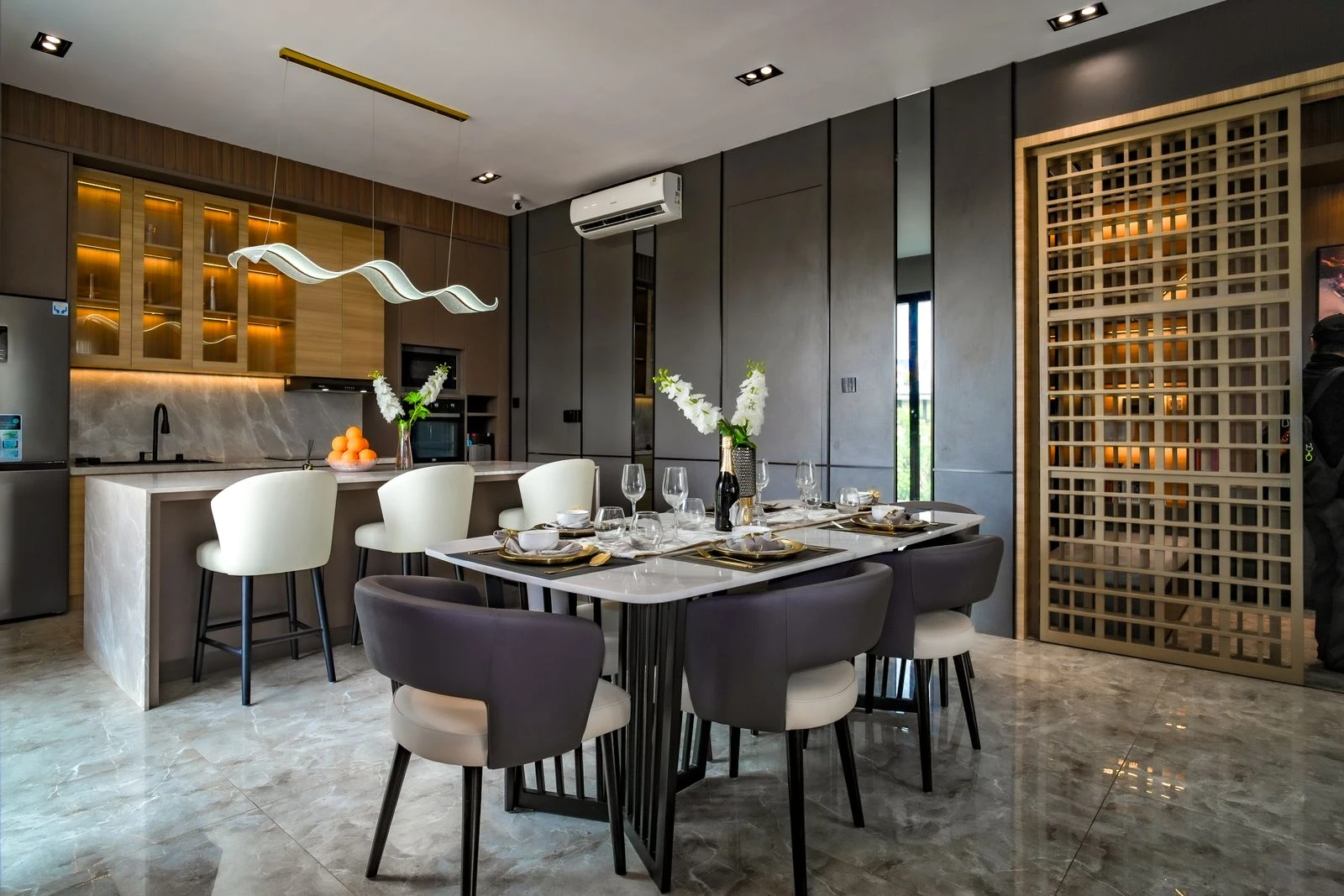 Open-plan dining and kitchen with a brass screen, stone floor and sculptural pendant lighting